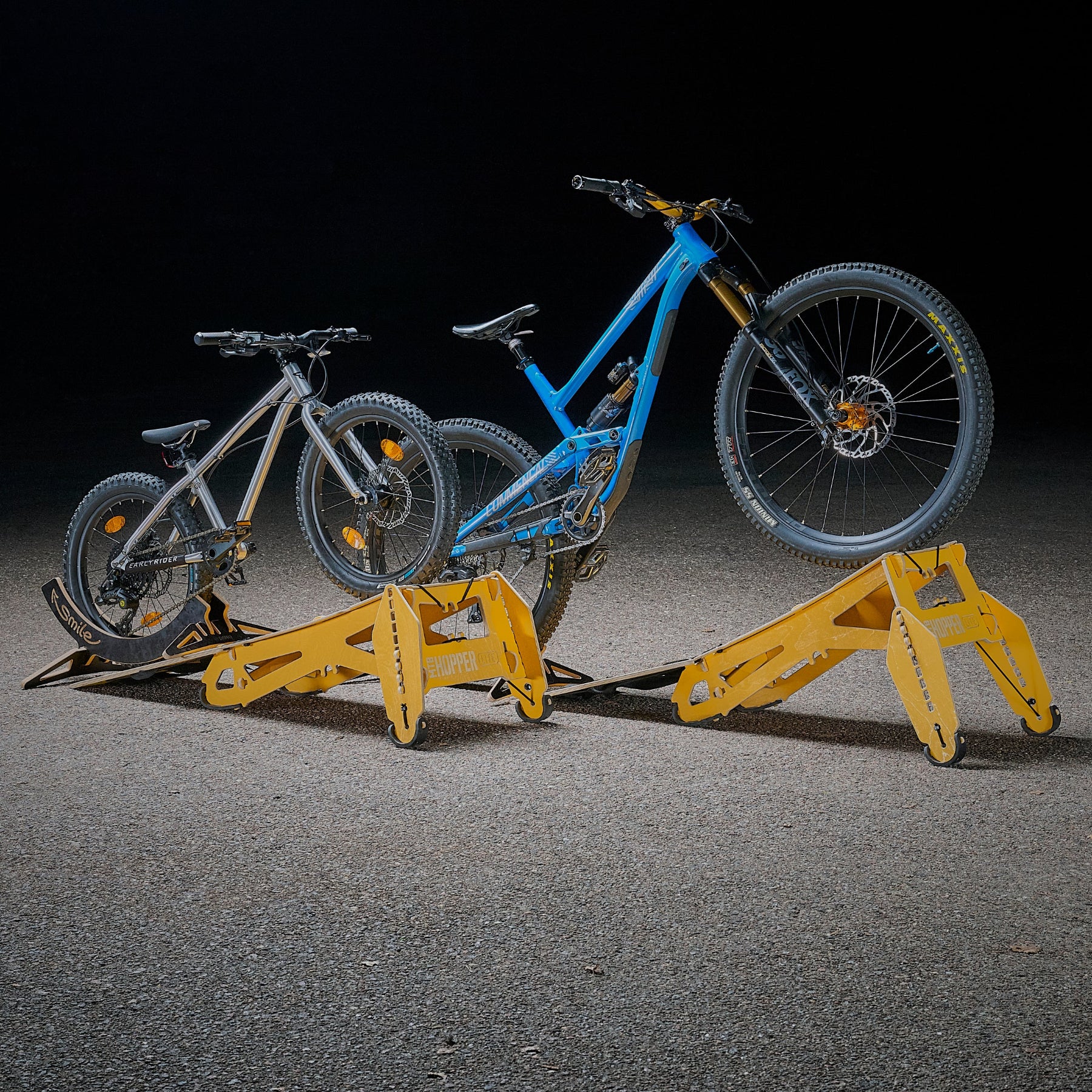 Two mountain bikes, one blue and one gray, are positioned on a yellow bicycle MTB Hopper ramp, which is designed for spot hunting and urban explorations.